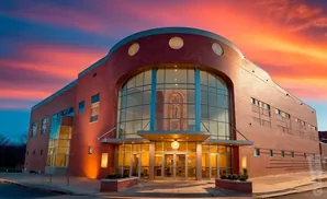 Brick building with a large arched window and colorful sunset sky.