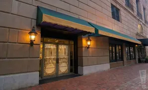Exterior of a building with a green awning, ornate double doors, and decorative wall lamps.
