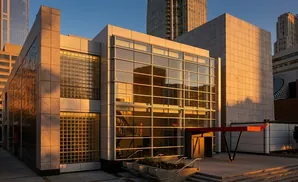 Modern building with glass and stone facade, bathed in golden hour light, reflecting a staircase.
