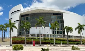 Modern white arena with a curved facade, large glass windows, and palm trees under a blue sky.