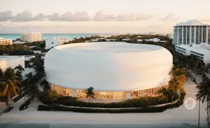 Modern white domed building surrounded by palm trees and ocean view.