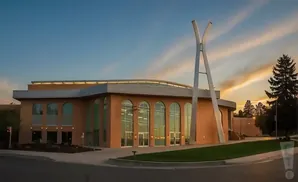 Modern building with arched windows and a tall, abstract sculpture at sunset.
