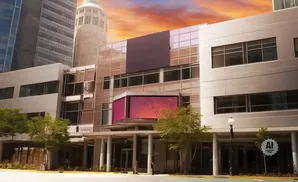 Modern office building with glass facade and large digital display, set against a colorful sky.