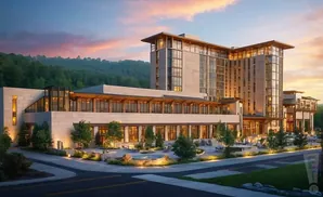 Modern hotel with stone facade and large windows at sunset, with trees and a courtyard.
