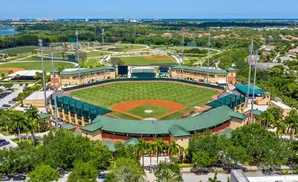 Aerial view of a baseball stadium surrounded by trees and a distant cityscape.