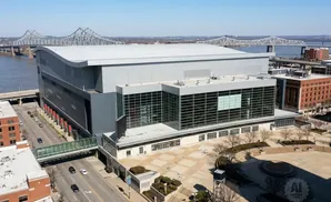 Aerial view of a modern arena with a river and bridge in the background.