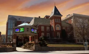 A red brick building with a tower and a modern glass addition, with digital billboards displaying colorful graphics.