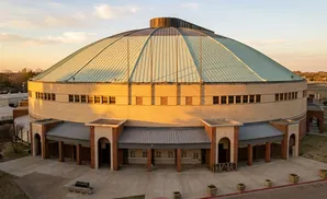 An aerial view of a large, circular building with a teal domed roof and beige brick exterior.