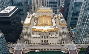 Aerial view of a large, ornate building with a gold roof, surrounded by tall skyscrapers and a river.
