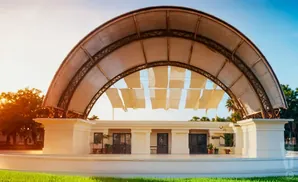 An outdoor stage with a large arched canopy, decorated with fabric panels, under a bright sky.