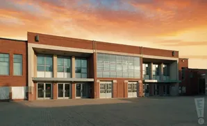 A modern brick building with large windows and glass doors under a dramatic sunset sky.