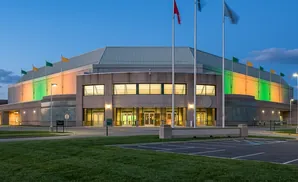 Large modern arena lit with colorful lights and flags flying high, at dusk.