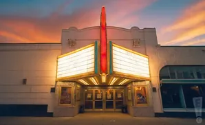 A vintage theater marquee glows against a colorful sunset sky.