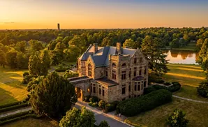 Stone mansion at sunset with a lake and trees.