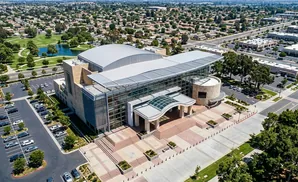 Aerial view of a modern building with a glass facade, surrounded by parking lots, trees, and residential neighborhoods.