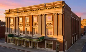 Exterior of a brick building with classical columns and arched windows, bathed in golden sunset light.