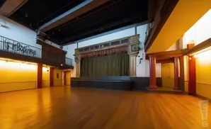 Empty, sunlit ballroom with stage and balcony.