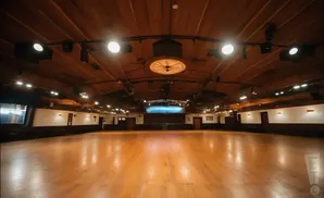 A large, empty ballroom with a polished wooden floor and a wooden ceiling with exposed beams and lights.