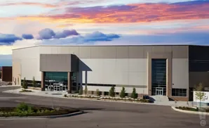 Modern warehouse building with large glass entrance under a dramatic sunset sky.