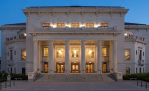 Grand neoclassical building with columns and large windows, illuminated at dusk.