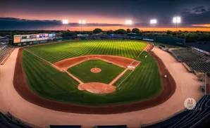 A baseball stadium at sunset, with bright lights illuminating the field and a colorful sky.