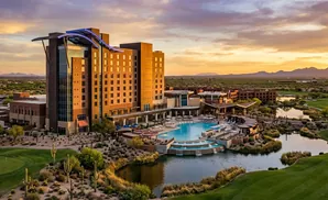 A modern resort hotel with a large pool sits on a golf course at sunset.