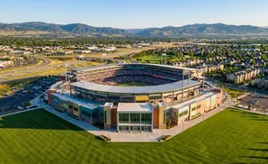 Aerial view of a baseball stadium filled with fans, surrounded by residential areas and mountains under a clear blue sky.