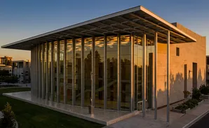 Modern building with glass facade reflecting trees and golden sky.