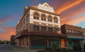 A historic brick building with arched windows stands under a vibrant orange sunset.