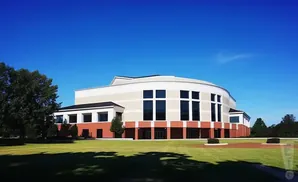 A large, modern building with a curved facade and large windows, set against a clear blue sky.