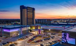Aerial view of a casino at sunset with a tall hotel tower and illuminated buildings.