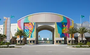 Brightly colored archway entrance to a fairground with flags and palm trees.