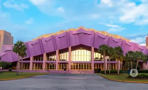 A large, modern purple building with a wavy roof and palm trees in front.