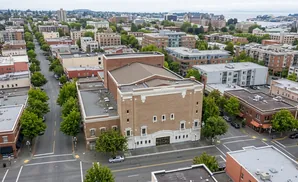 Aerial view of a street lined with brick buildings and trees, leading to a large theater.