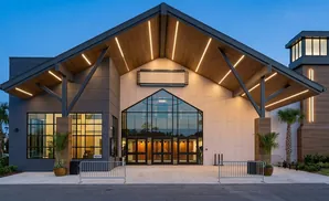 Modern building entrance with large glass doors and a pitched wooden roof with integrated lighting.