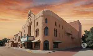 A tan adobe building with an ornate facade and marquee stands under a vibrant orange sky.
