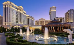 Fountains and lush gardens in front of a grand Roman-style hotel and casino at dusk.