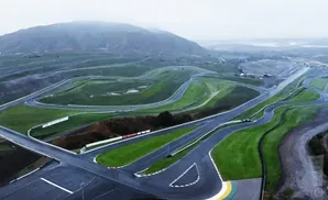 Aerial view of a winding race track through rolling green hills under a hazy sky.