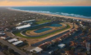 Aerial view of a horse racing track and surrounding buildings, with the ocean in the background.