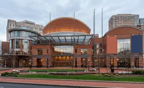 Modern brick theater building with a domed roof, large glass windows, and surrounding trees.