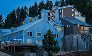 A modern, multi-level blue and brown building nestled into a hillside forest.
