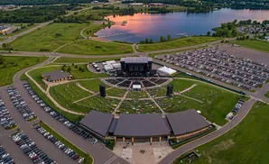 Aerial view of an outdoor amphitheater concert, with a lake in the background and large parking lots.