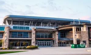 Modern stadium entrance with stone facade, large windows, and a curved roof.