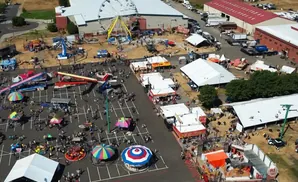An aerial view of a busy fairground with rides, tents, food stalls, and many people.