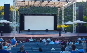 Outdoor movie screen with tiered seating for an audience in a natural setting.