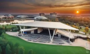 An outdoor amphitheater at sunset with surrounding buildings and a lake.