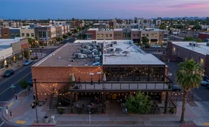 Aerial view of a modern brick building with outdoor seating and string lights at dusk.