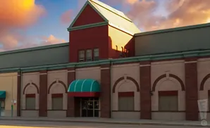 A red and tan building with a teal awning over the entrance, under a colorful sunset sky.