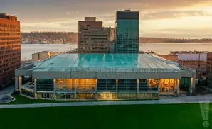 A modern building with a glass roof and facade on a waterfront at sunset.