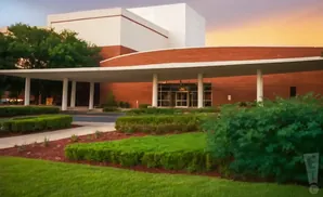 A modern brick building with white accents and a covered entrance, surrounded by manicured hedges and green grass.